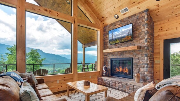 A wooden interior with a fireplace, large windows, and a view of mountains. - Southern Stars (Gatlinburg)