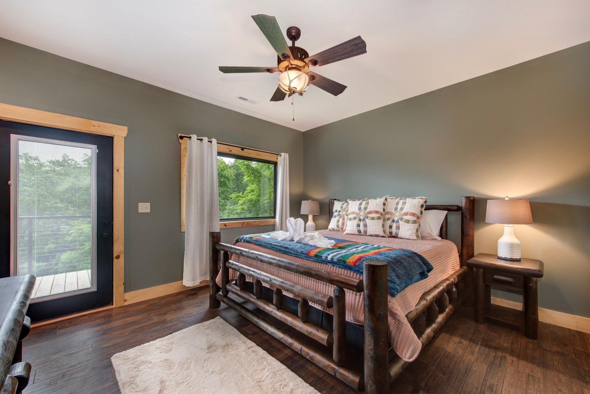 A bedroom with a bed, a ceiling fan, a window, a door, and a nightstand with a lamp.