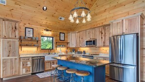 Cocina de cabaña de madera con una isla central, electrodomésticos de acero inoxidable y taburetes de bar.