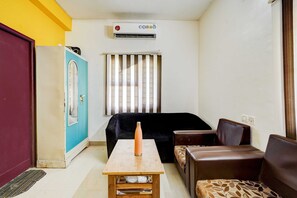 A compact room with a bed, a table with a bottle, a sofa, a cabinet, and an air conditioning unit. - Collection O Kelambakkam Chennai (Tirupporur)