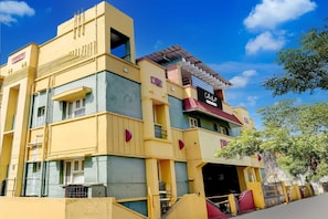 A multi-story building with a yellow facade, balconies, and a storefront with a sign. - Collection O Kelambakkam Chennai (Tirupporur)