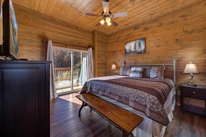 A wooden cabin bedroom with a bed, bench, ceiling fan, and a painting on the wall. - Majestic Overlook (Gatlinburg)