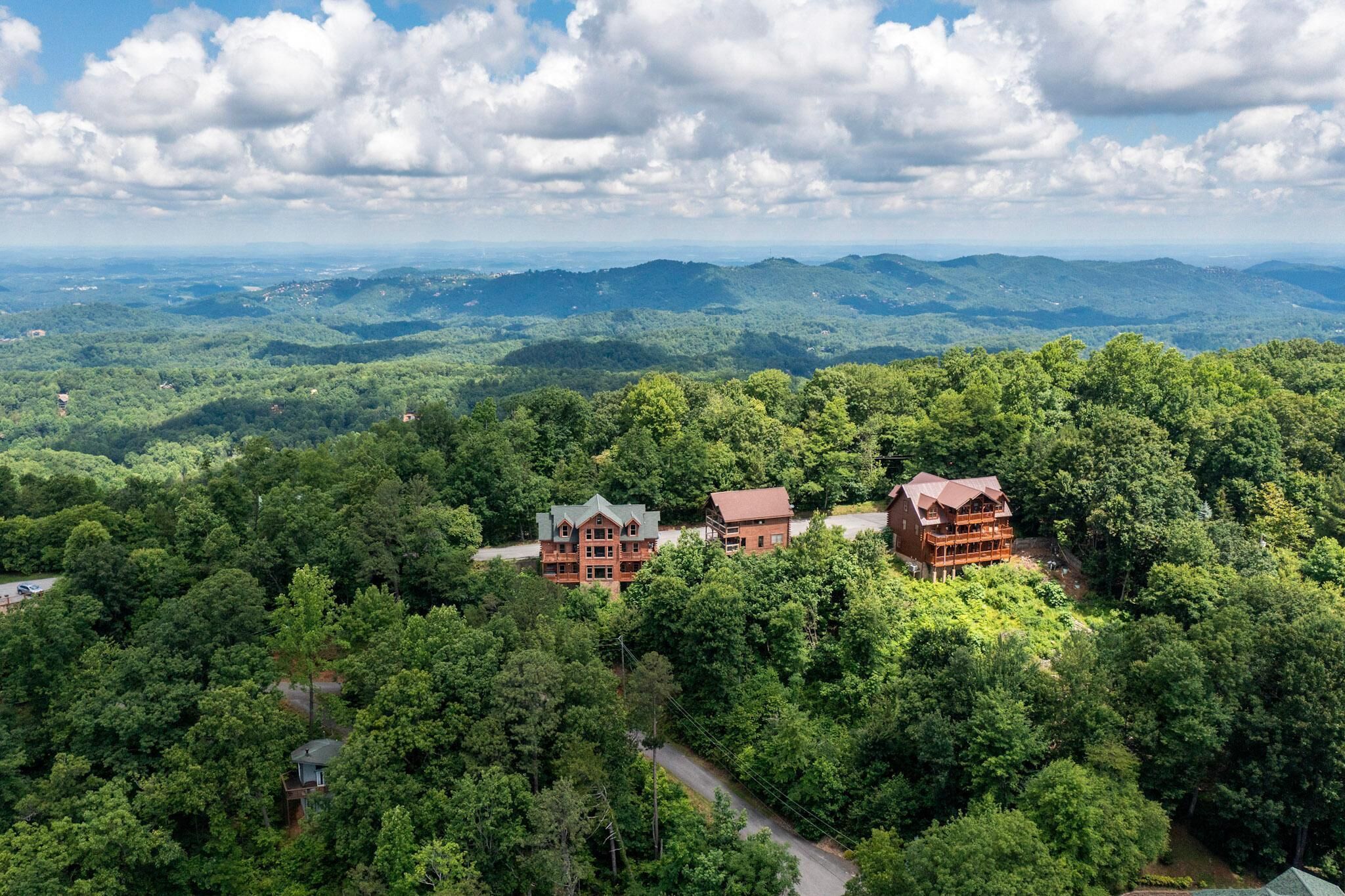 A lodge with multiple buildings surrounded by dense forest, with a view of distant mountains.