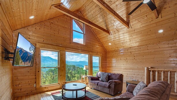 A wooden cabin interior with a sofa, armchair, and a round table. - Papa Bears Magnificent View (Gatlinburg)