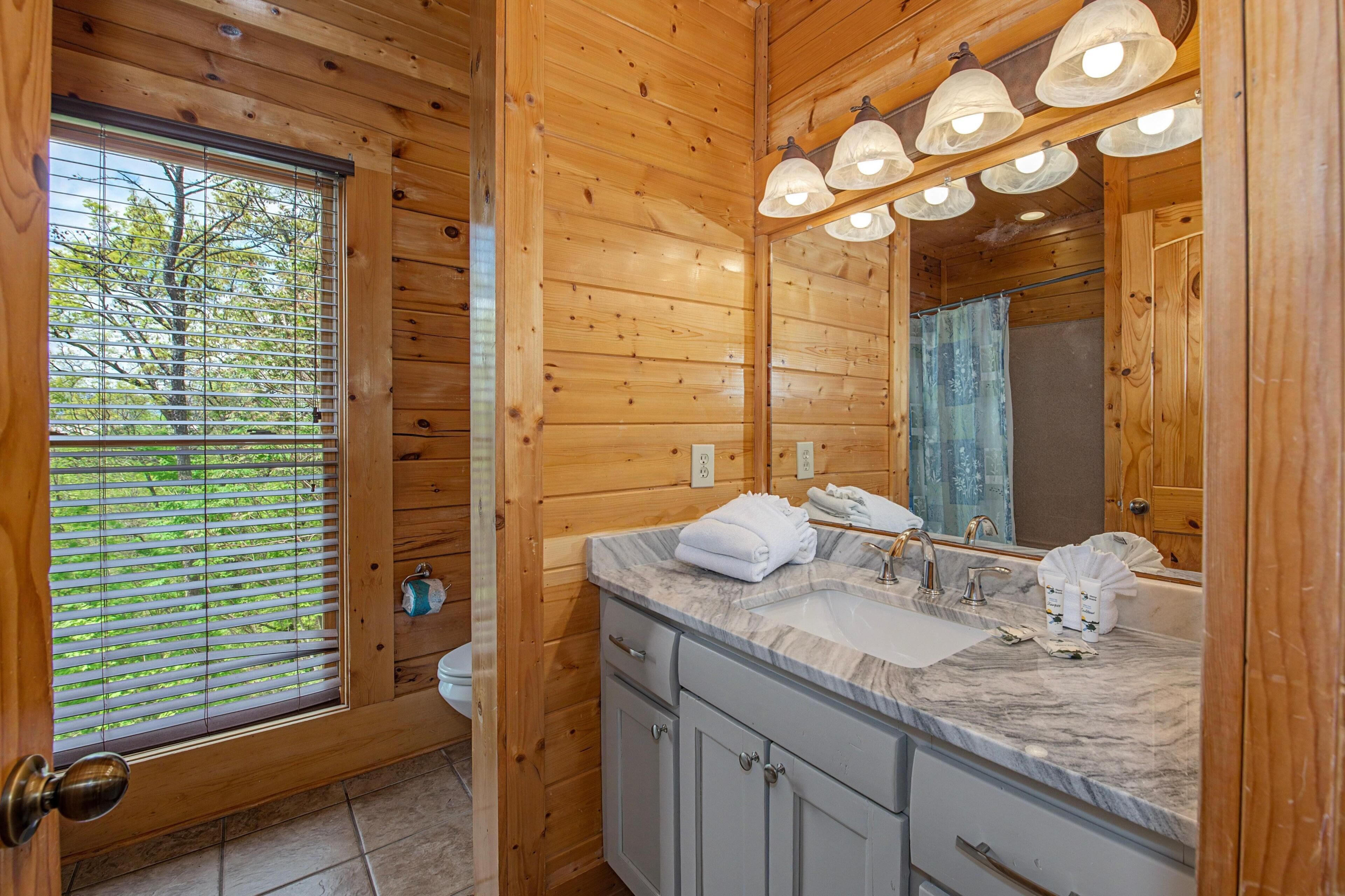 A wooden cabin bathroom with a large window, a sink with a mirror, and a shower area.