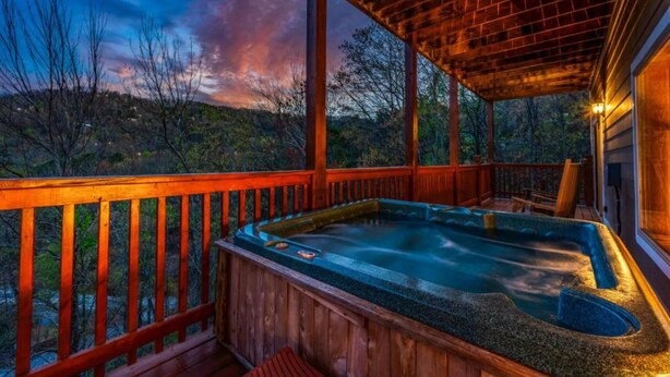 Ein Whirlpool auf einer Holzterrasse mit Blick auf Bäume und Hügel.