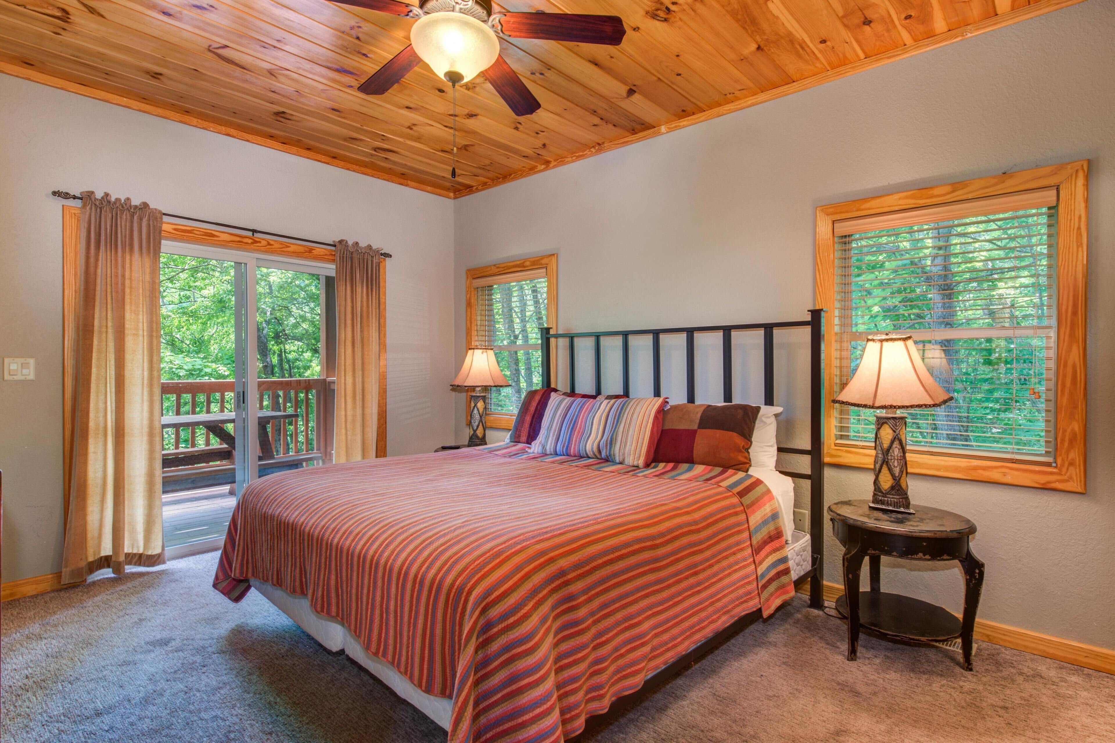 A bedroom with a bed, two windows, a ceiling fan, and a nightstand with a lamp.