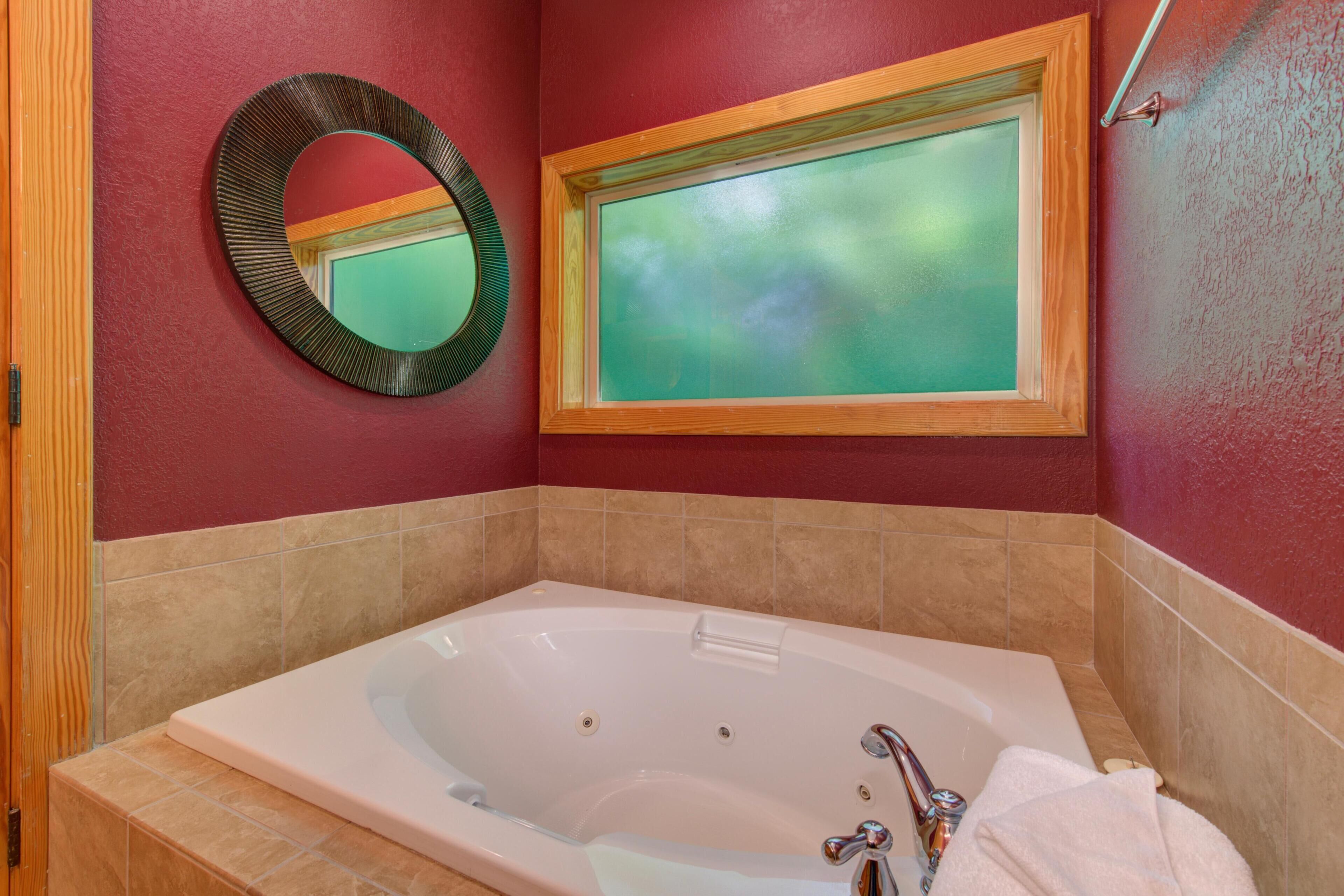 A bathroom with a large bathtub, a round mirror, and a window with a view.
