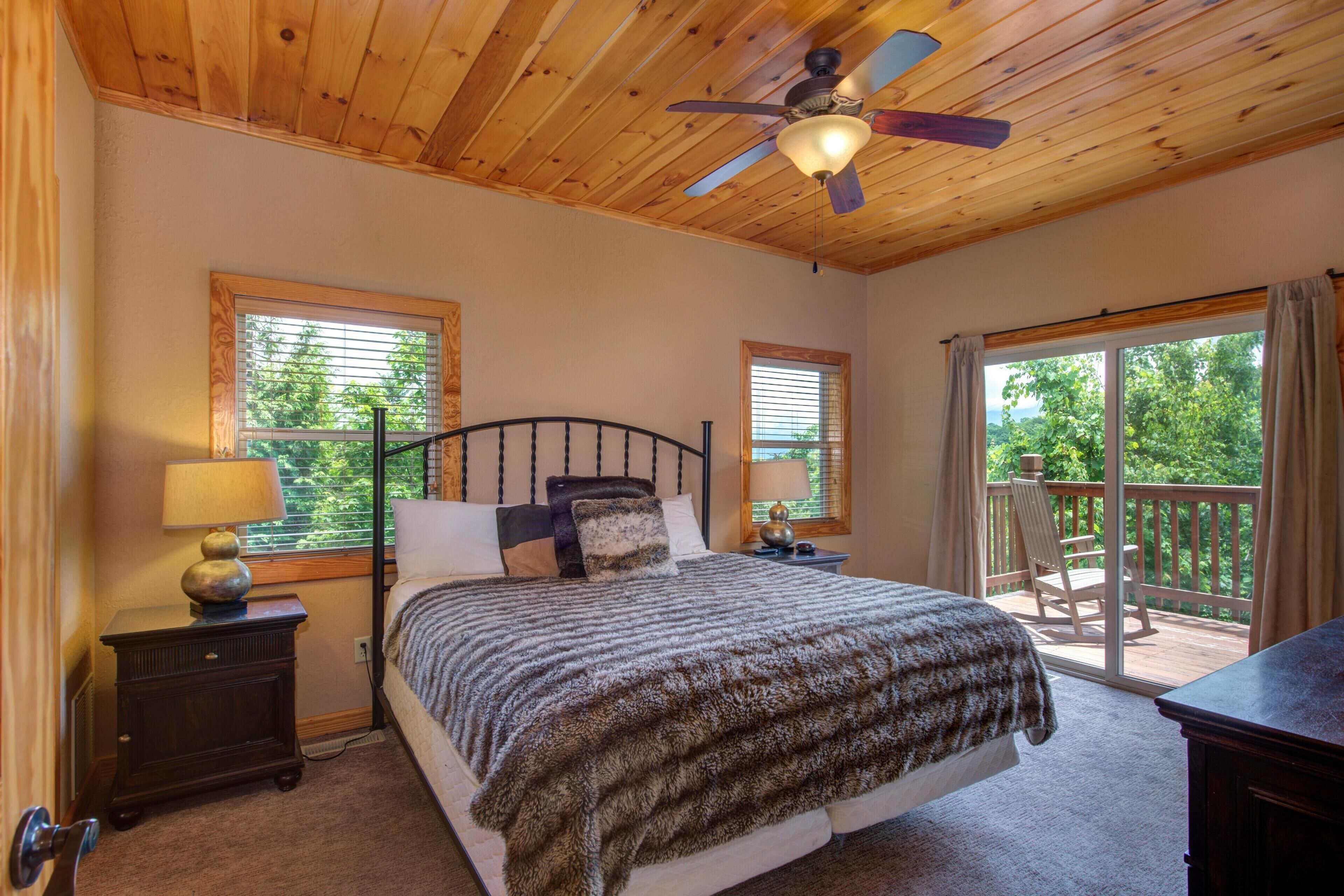 A bedroom with a bed, a nightstand, a lamp, a ceiling fan, and a balcony with a chair.