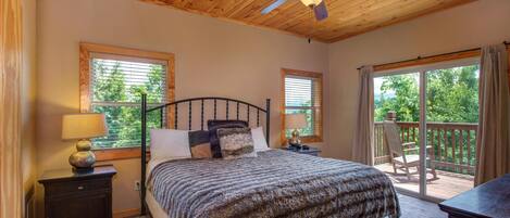 A bedroom with a bed, a nightstand, a lamp, a ceiling fan, and a balcony with a chair.