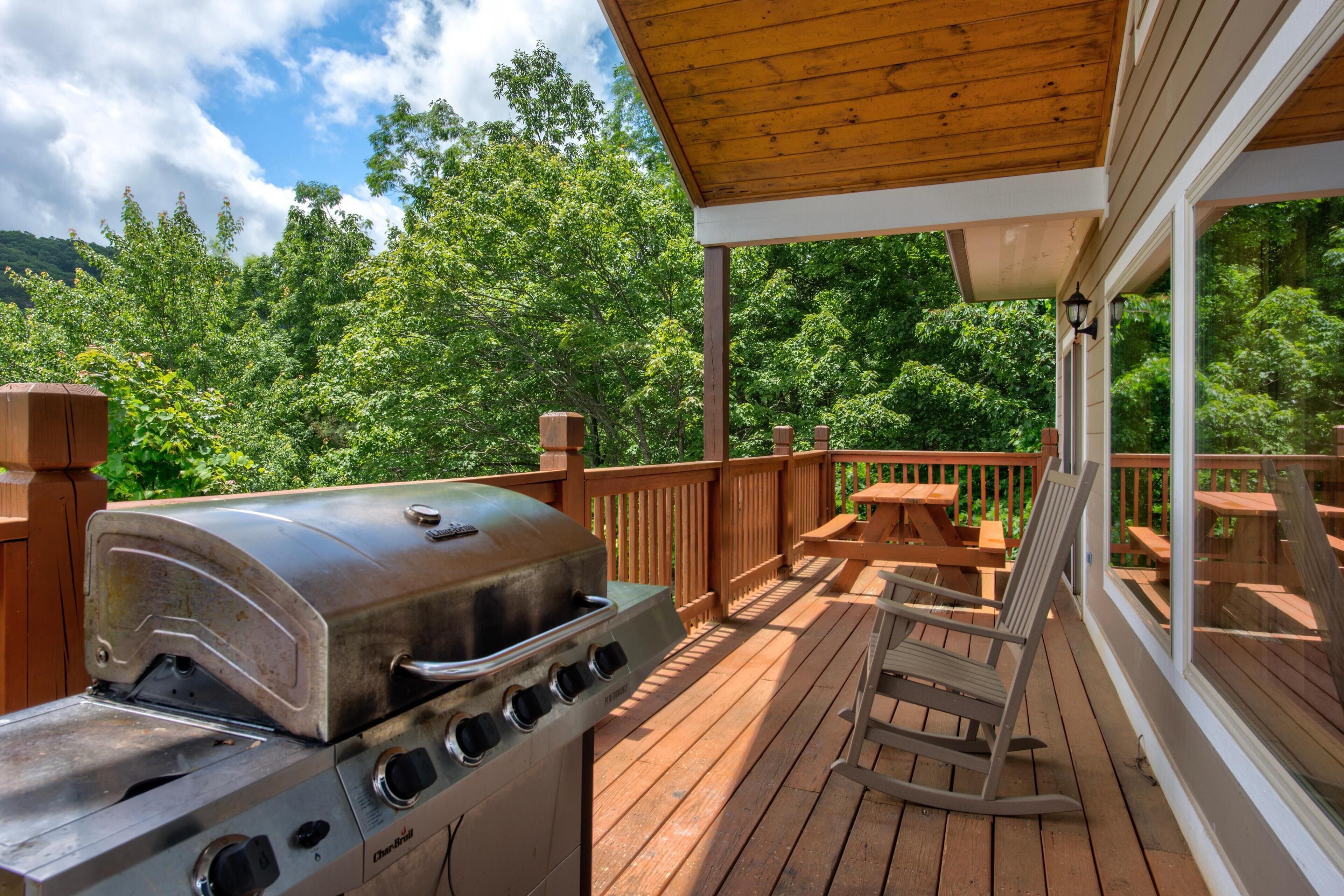Una terraza de madera con una parrilla, una mecedora y una mesa.
