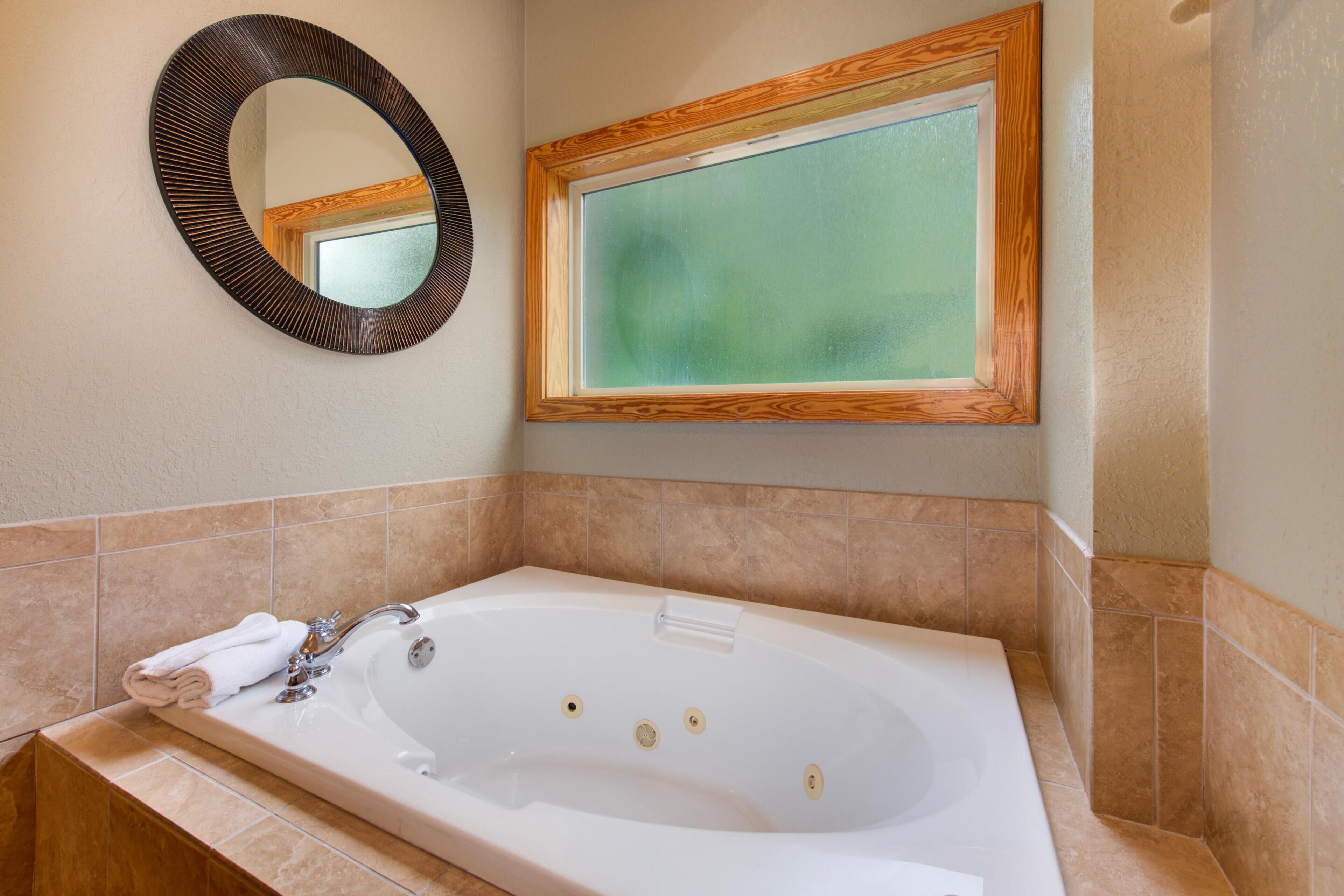 A bathroom with a large bathtub, a mirror, and a window.