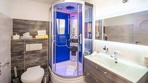 Et moderne badeværelse med en brusekabine i glas, et hvidt toilet, et spejl og en vaskebord med vask.