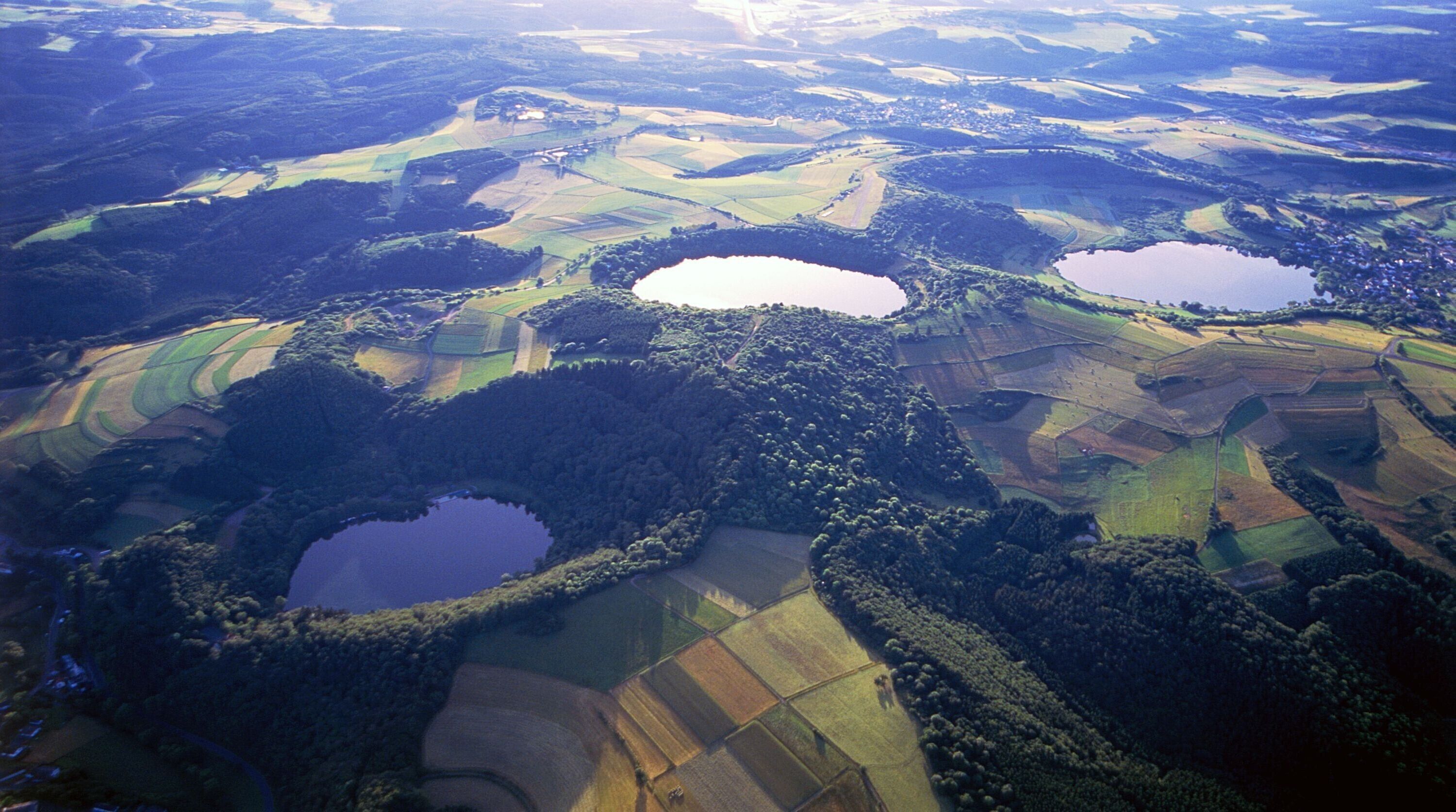 An aerial view of a rural landscape with three distinct water bodies surrounded by terraced fields and dense forests.