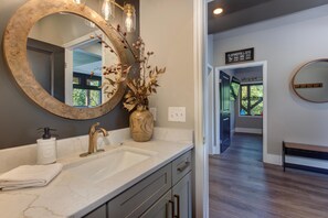 A bathroom with a large mirror, a sink, and a vase with dried branches. - The Ember (Gatlinburg)