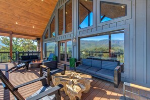 Une vaste terrasse dotée d’un espace salon extérieur, d’un foyer et de grandes fenêtres offrant une vue sur les montagnes.