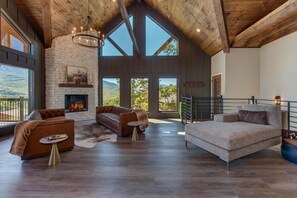 A spacious living area with a fireplace, leather sofas, and large windows offering mountain views. - The Ember (Gatlinburg)