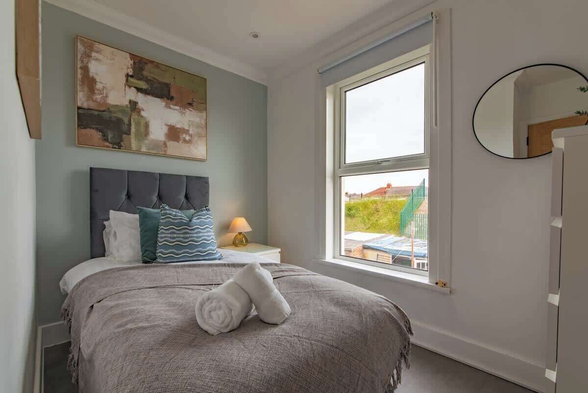 Une chambre à coucher avec un lit, une fenêtre, une table de chevet avec une lampe et un miroir fixé au mur.