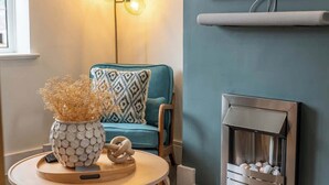 Ein gemütliches Wohnzimmer mit einem blauen Sofa, einem gemusterten Zierkissen, einer Dekovase, einem Kamin und einem an der Wand montierten Fernseher.