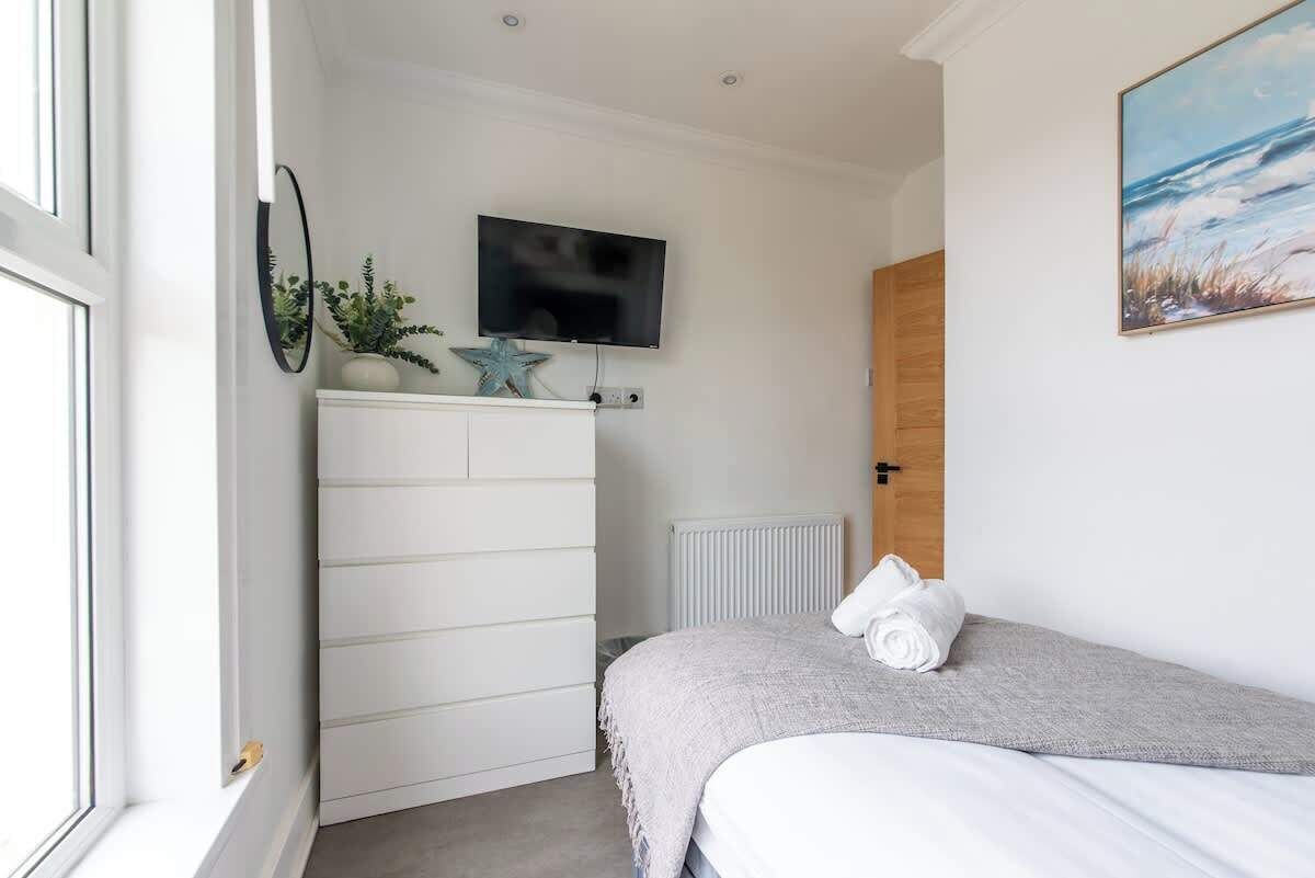 A bedroom with a bed, a TV mounted on the wall, a radiator, and a window.