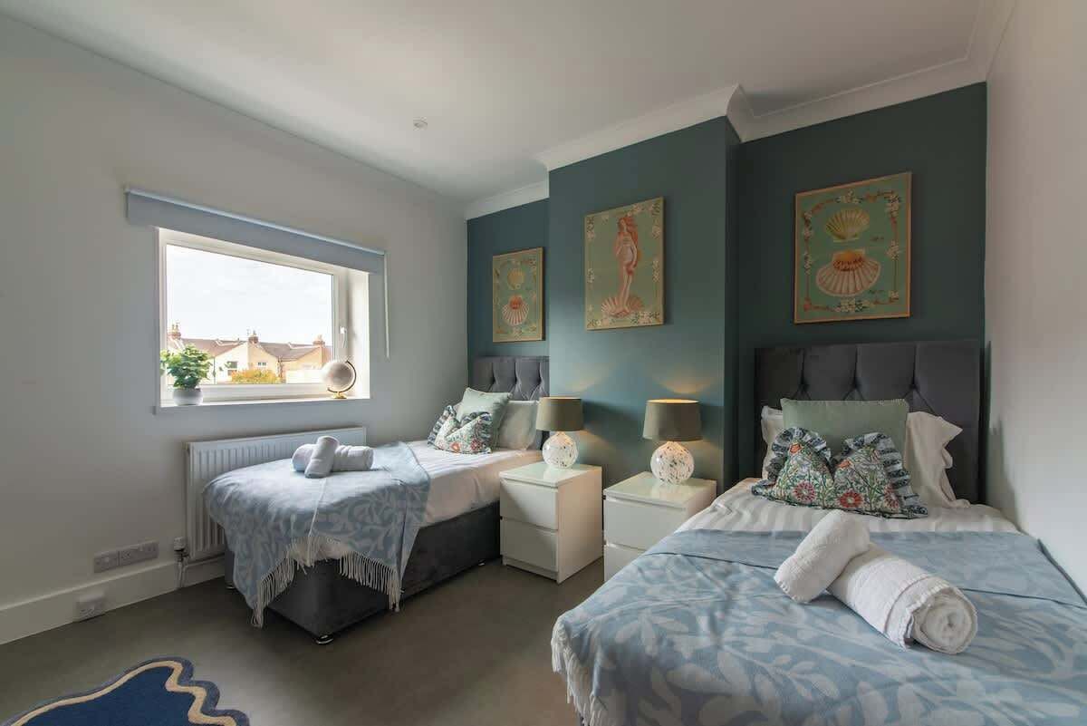 A bedroom with two beds, a window, and artwork on the walls.