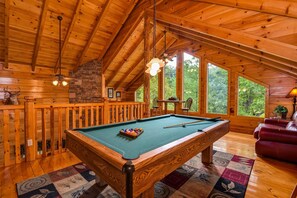 A wooden interior with a pool table, a stone wall, and large windows. - One More Night (Sevierville)