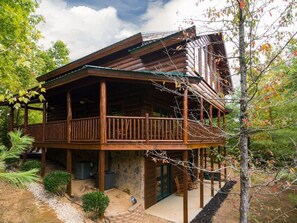 A wooden cabin with a balcony, stone foundation, and a small garden area. - One More Night (Sevierville)