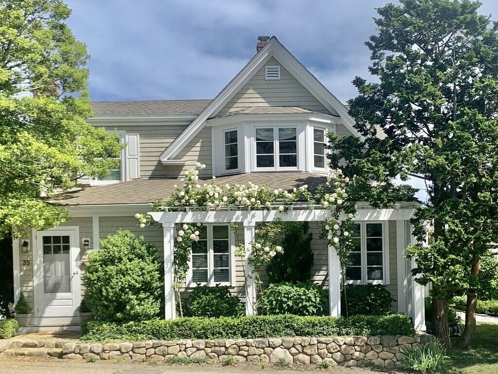 A two-story house with a stone foundation, a porch with white columns, and a covered entryway.