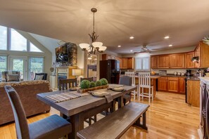 A spacious kitchen with wooden cabinets, a dining table set with plates and a centerpiece, and a large window providing natural light. - Palmer's Place (Sevierville)