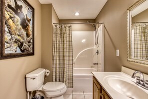 A bathroom with a toilet, sink, shower, and a painting on the wall. - Palmer's Place (Sevierville)