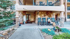 A building with a stone facade, a balcony with blue railings, and outdoor seating with chairs and a decorative figure. - Riverside Escape (Gatlinburg)