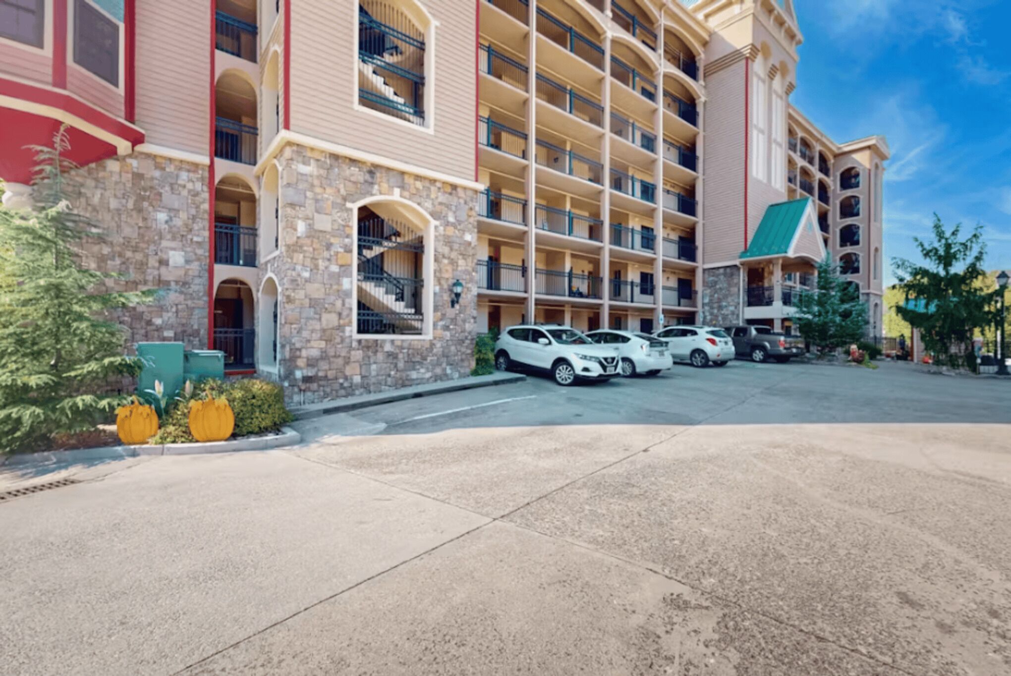 Ein mehrstöckiges Hotel mit einer Stein-Fassade, Balkonen und einem Parkplatz mit mehreren Autos.