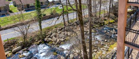 A view of a river with rocks and trees, a road, and a building with a balcony.