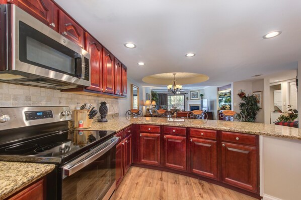 A kitchen with a stainless steel microwave, a stove, wooden cabinets, granite countertops, and a chandelier. - Riverside Escape (Gatlinburg)