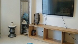 Ein modernes Wohnzimmer mit einem an der Wand befestigten Flachbildfernseher, einer Holz-Unterhaltungsecke darunter, einem dekorativen Spiegel und einem Teppich im Strandhaus-Stil.