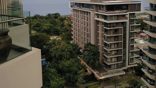 Ein Hochhaus mit mehreren Balkonen, Blick aufs Meer und umgebender Bepflanzung.