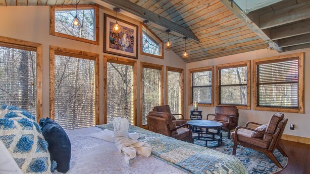 A room with a large bed, a dining table, and multiple windows. - Cricket Hollow Lodge (Cosby)