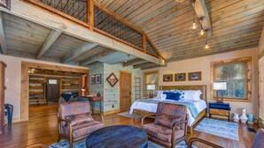 A spacious room with a high ceiling, a large bed, multiple seating areas, and a view of the outdoors. - Cricket Hollow Lodge (Cosby)