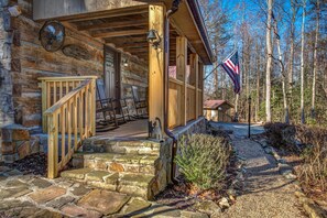 A log cabin with a stone staircase, wooden porch, and an American flag. - Cricket Hollow Lodge (Cosby)