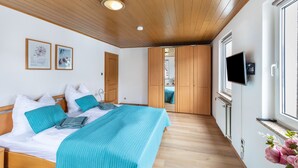 Une chambre à coucher avec un lit, un plafond en bois, un téléviseur fixé au mur et une fenêtre.