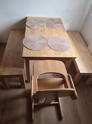 A wooden table with four woven placemats and a wooden chair.