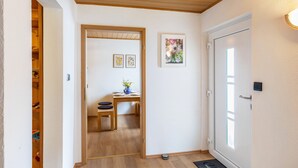 Un couloir avec une porte en bois, une petite table sur laquelle se trouve un vase, et un interphone.