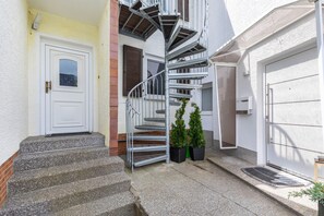 A residential building with a spiral staircase leading to a second-floor landing, a white door, and a garage door.
