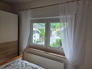 A bedroom with a window, a radiator, and a bed with a patterned bedspread.