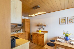Una cocina con armarios de madera, microondas y comedor con mesa para dos.