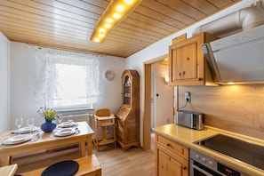 A modern kitchen with wooden cabinets, a built-in oven, a microwave, and a dining area with a table set for two.