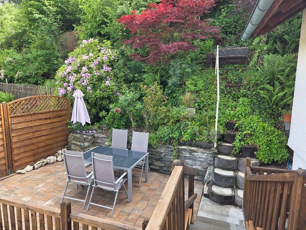 An outdoor patio with a table and chairs, surrounded by a wooden fence and lush greenery.