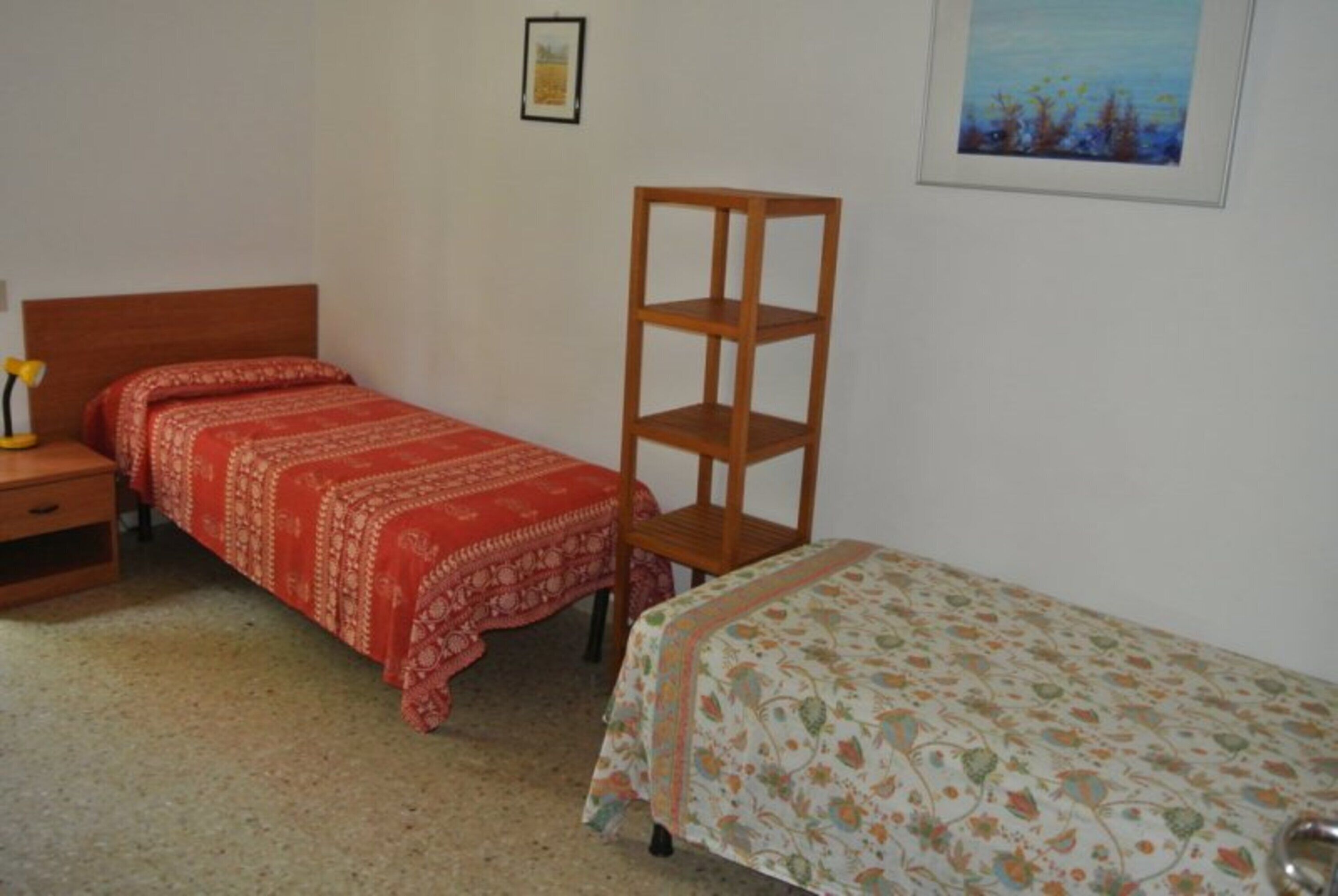Une chambre avec deux lits simples, une table de chevet en bois, une petite table et une étagère fixée au mur.