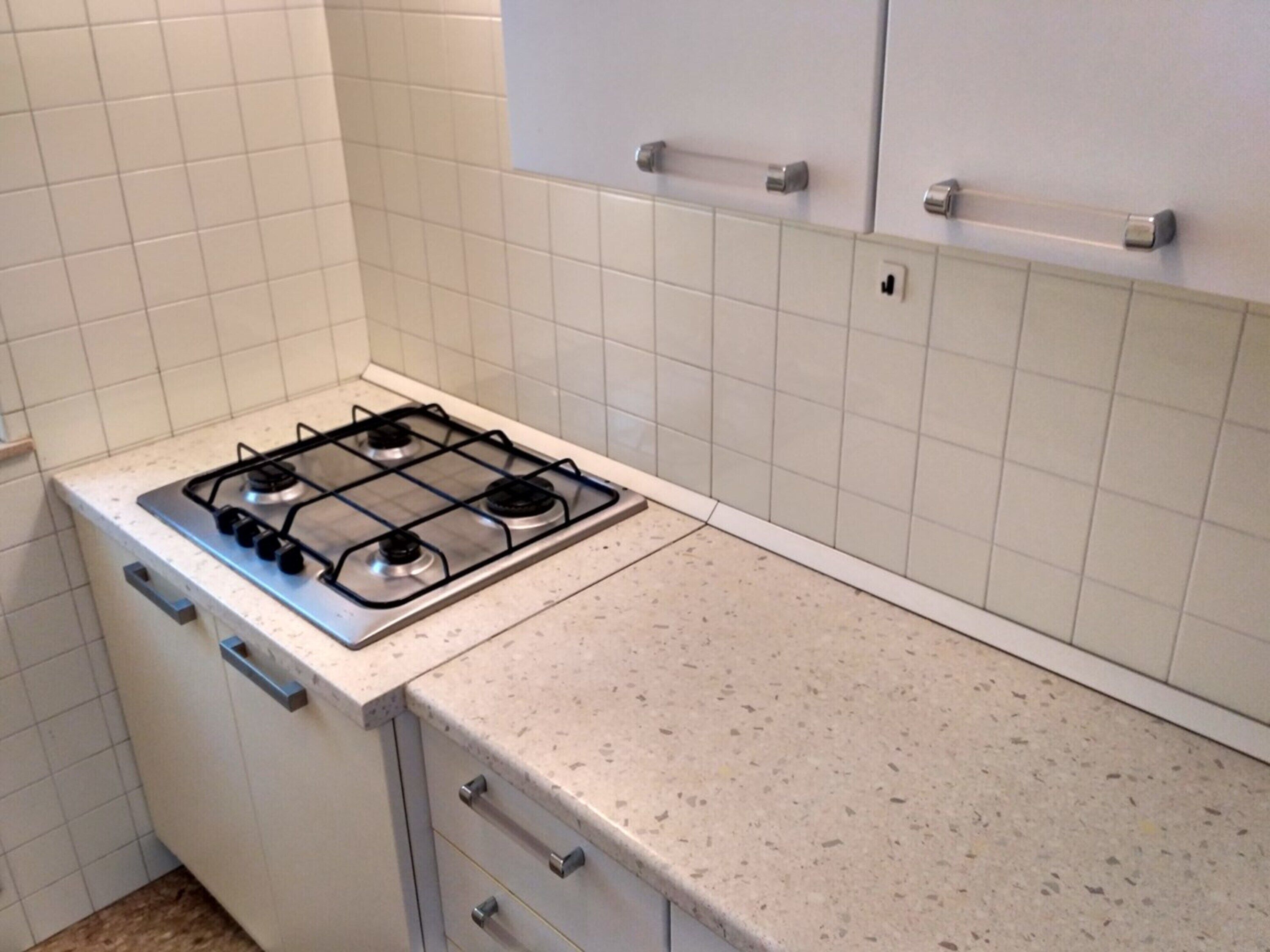 A kitchen with a gas stove, white cabinets, and a speckled countertop.