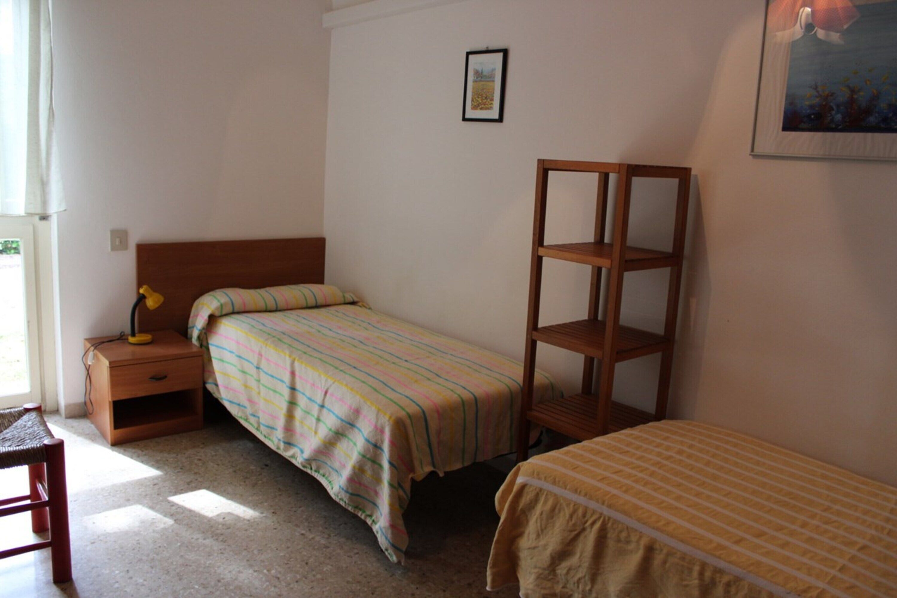 Een slaapkamer met een enkel bed, een nachtkastje met een lamp, een houten plank en een kleine tafel.